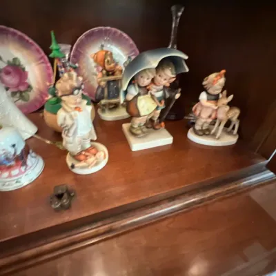 Collection of vintage porcelain figurines, including Hummel-style children with an umbrella and deer, displayed inside a wooden cabinet...
