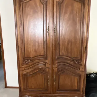 French Provincial style carved wooden armoire featuring double panel doors with ornate brass hardware and cabriole legs.