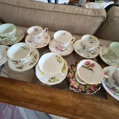 Collection of assorted vintage floral porcelain teacups and matching saucers displayed on a glass-top table.