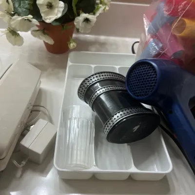 Collection of bathroom and household accessories, including a blue hair dryer, a plastic drawer organizer, a decorative cup, and a potted...