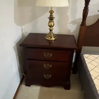 Traditional dark wood nightstand with brass hardware, featuring a polished brass table lamp with a pleated shade.