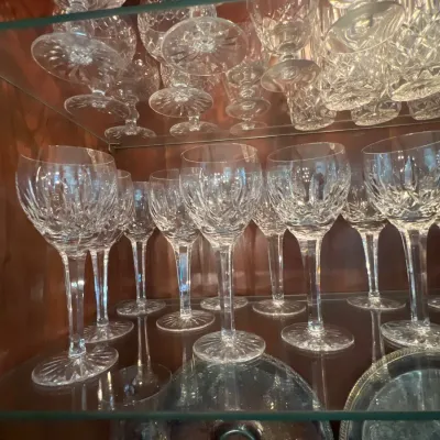 Collection of cut crystal wine glasses and glassware displayed on glass shelves inside a wooden hutch.