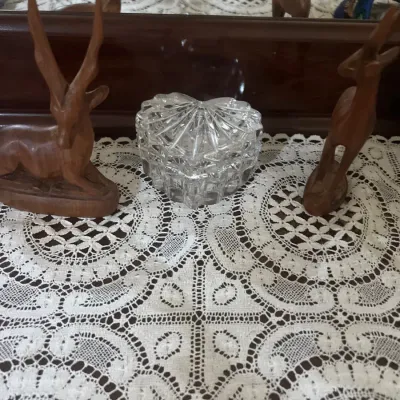 Heart-shaped lead crystal trinket box flanked by carved wooden antelope figurines, displayed on a lace table runner.