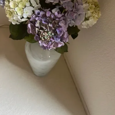 Arrangement of artificial hydrangea stems in purple, lavender, and cream tones set inside a frosted glass vase.