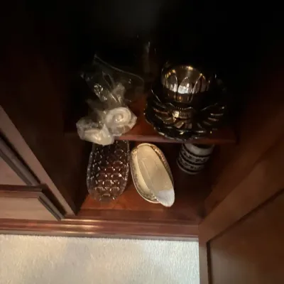 Selection of glassware and silver-tone serving pieces stored inside a dark wood cabinet shelf.