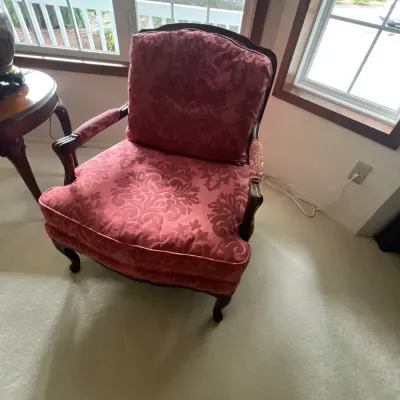 French Provincial style armchair featuring a carved dark wood frame, padded armrests, and plush pink damask fabric upholstery.
