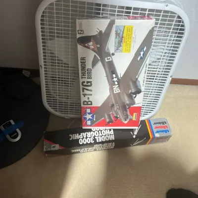A collection of household items including a vintage white box fan, a Lindberg B-17G Thunderbird model airplane kit, and a boxed Albinar...