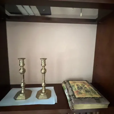 Pair of vintage brass baluster-style candlesticks displayed on a shelf alongside a decorative book featuring a portrait cover illustration.