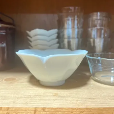 Collection of kitchenware, including a white porcelain flower-shaped bowl, clear glass dessert dishes, and a brown ceramic crock on a...