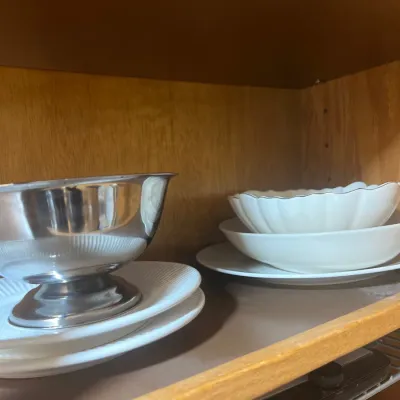 Selection of serveware including a silver-tone footed bowl on white porcelain plates and stacked fluted white ceramic dishes.