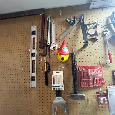 Assortment of hand tools hung on a pegboard wall, including pipe wrenches, adjustable wrenches, levels, a hammer, funnels, and a hex key...