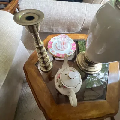 Collection of tabletop decor including a brass candlestick, porcelain teapot, decorative saucers, and a lamp resting on a hexagonal...