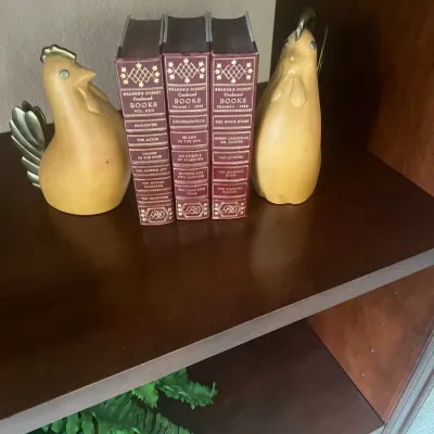 Pair of carved wooden chicken bookends with brass accents flanking three vintage Reader's Digest Condensed Books from the 1950s.