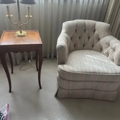 Vintage tufted barrel armchair with pastel striped upholstery alongside a cabriole-leg wooden side table and two-light brass table lamp.