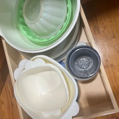 Collection of vintage Tupperware plastic kitchenware, including a Jel-Ring mold and serving bowls, stored inside a wooden drawer.