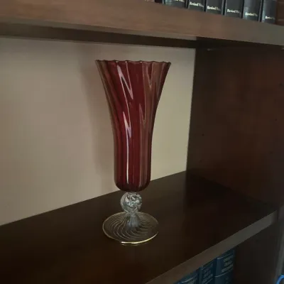 Tall ruby red blown glass vase featuring a swirl pattern, twisted clear glass knop, and round foot rimmed in gold.