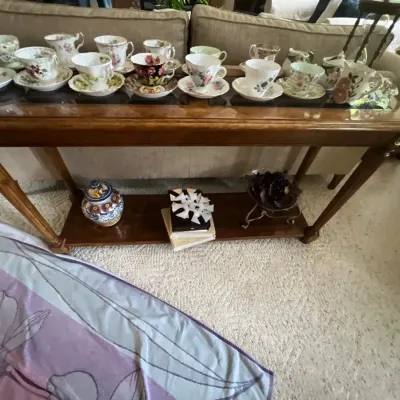 Collection of vintage porcelain teacups and saucers arranged on a wooden console table with a lower shelf.