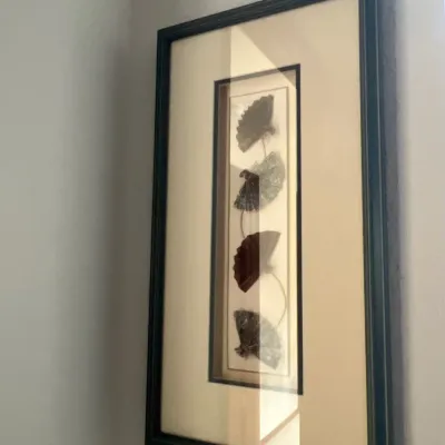 Framed wall art featuring a vertical arrangement of decorative mini folding fans in a dark molded frame.