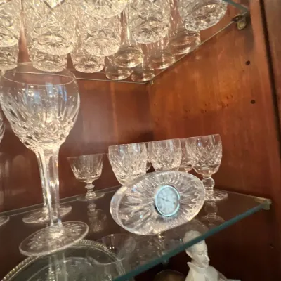 Collection of cut crystal glassware, including wine goblets, short-stemmed glasses, and a crystal desk clock displayed on a glass cabinet...