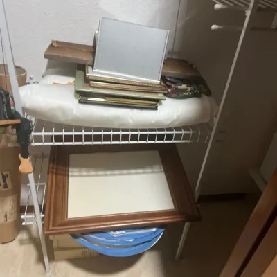 Assorted picture frames, including a large wooden wall frame and various smaller desk and wall frames, stored on closet shelving.