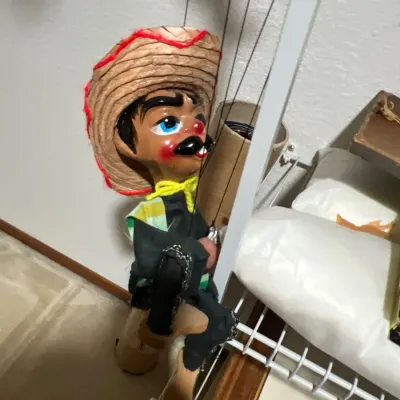Vintage Mexican marionette string puppet wearing a straw sombrero, yellow neckerchief, and black charro outfit.