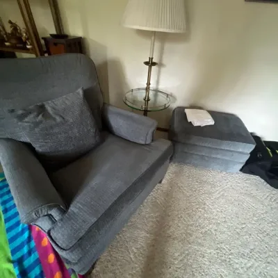 Gray upholstered armchair with matching throw pillow and ottoman, paired with a brass and glass floor lamp table.