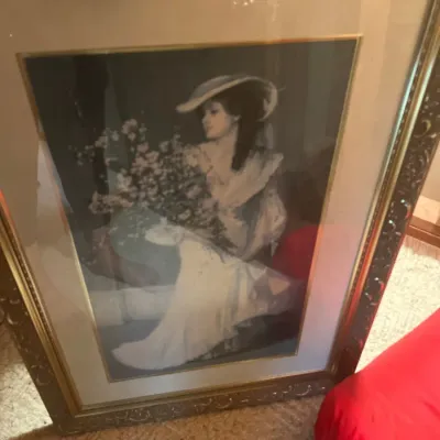 Framed vintage art print depicting a Victorian-style woman in a wide-brimmed hat holding a bouquet of flowers. Housed behind glass in a...