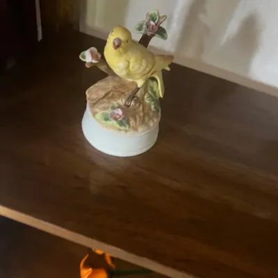 Vintage ceramic yellow bird music box featuring a songbird perched on a flowering branch base.