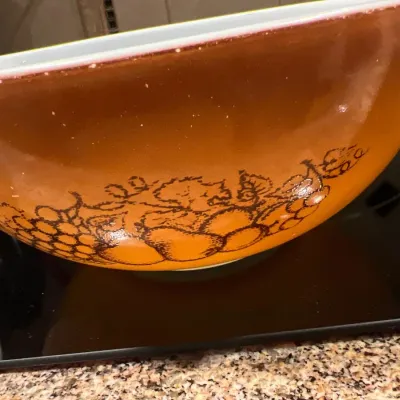 Vintage Pyrex Cinderella mixing bowl in the Autumn Harvest pattern, featuring a burnt orange gradient background with brown fruit...
