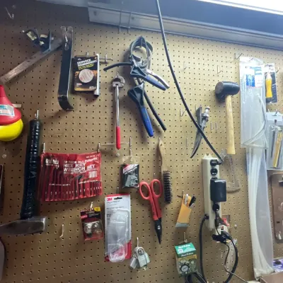 A pegboard wall organized with an assortment of hand tools, including hammers, pliers, hex keys, safety glasses, and a power strip.