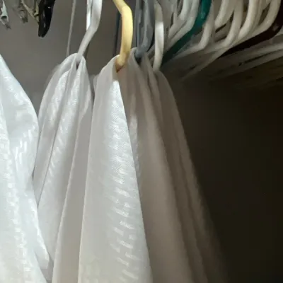 White patterned linens hanging on plastic clothes hangers in a closet.