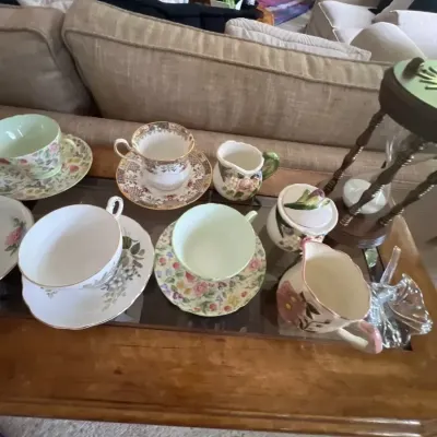 Collection of vintage floral bone china teacups, matching saucers, creamer pitchers, and a covered sugar bowl displayed on a wooden...