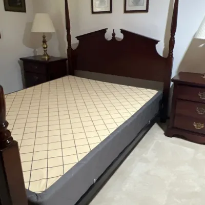 Traditional dark wood four-poster bed frame with a broken pediment headboard and urn finial, shown with a box spring. Flanked by matching...