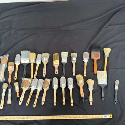 Large assortment of vintage and modern paintbrushes in various shapes and sizes, displayed with yardsticks for scale.