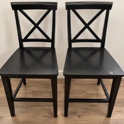 Pair of modern black wood dining chairs with x-back backrests, showing minor surface wear on one seat.