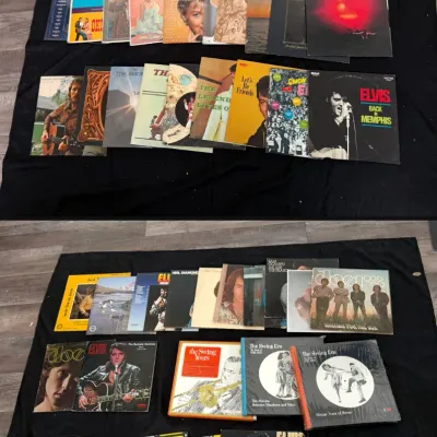Large collection of vintage vinyl LP records, sheet music, and box sets laid out on a black backdrop, featuring artists such as Elvis...