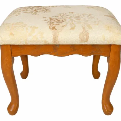 Vintage vanity stool or footrest featuring cabriole wood legs and a cream-colored floral jacquard cushioned top. Shows moderate finish...