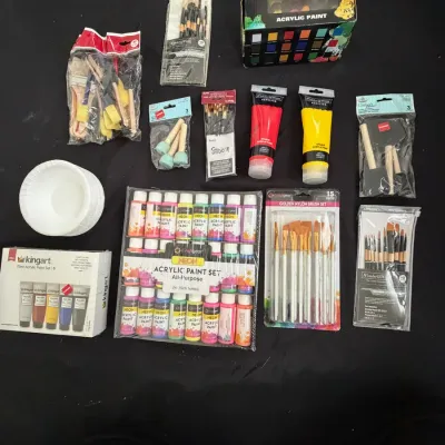 Assortment of art supplies including acrylic paint sets, neon paints, paint tubes, and various paintbrushes in foam, nylon, and detail...