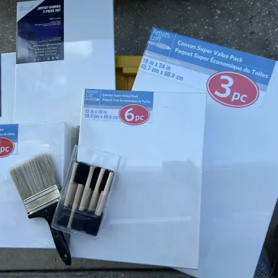 Assorted Artist's Loft stretch canvas multipacks and painting tools, including foam brushes and a wide flat paintbrush.