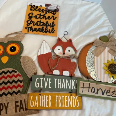 Collection of autumn and Thanksgiving-themed wall and door decorations, including a burlap owl, wooden fox, pumpkin sign, and metal...
