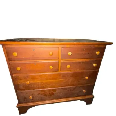 Vintage solid wood chest of drawers with round wooden knobs, keyhole accents, and a bracket base, showing surface wear and finish distress.