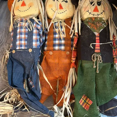 Trio of plush fabric fall scarecrow decorations with straw accents, wearing overalls and hats.