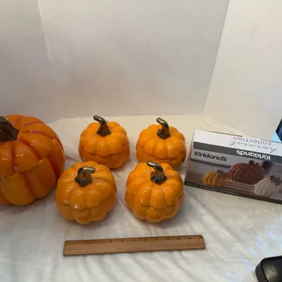 Collection of glazed ceramic pumpkin table decor, including a large pumpkin cookie jar and four small pumpkin lidded dishes, alongside a...
