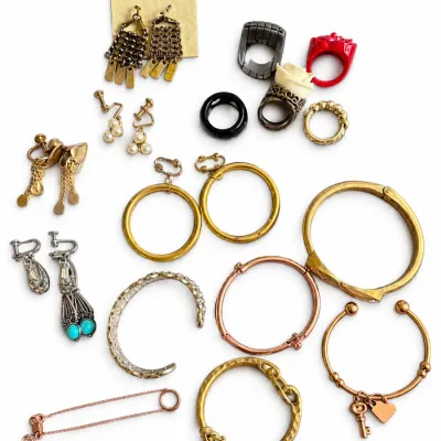Collection of vintage fashion jewelry including dangle earrings, clip-on hoop earrings, statement rings, and metallic bangles and bracelets.