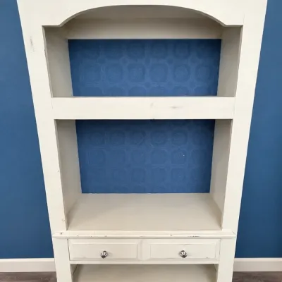 Off-white painted wooden bookcase or hutch with distressed finish, featuring arched top molding, open upper shelving, and two small...
