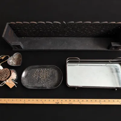 Collection of decorative tabletop items featuring a carved dark wooden shelf, a wire-framed mirrored vanity tray, a floral cast metal...