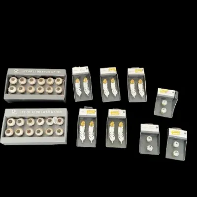 Collection of unused cabinet hardware in original retail packaging, including ceramic drawer knobs and feather-shaped pulls.