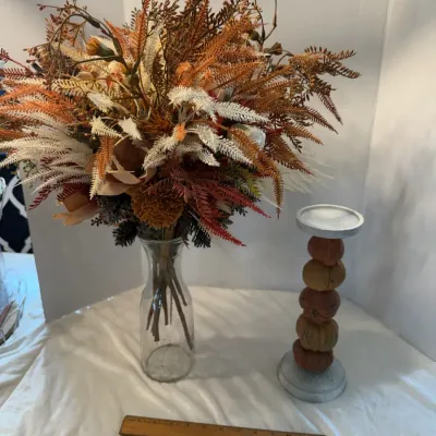 Autumnal faux floral arrangement in a clear glass vase displayed alongside a stacked pumpkin pillar candle holder.