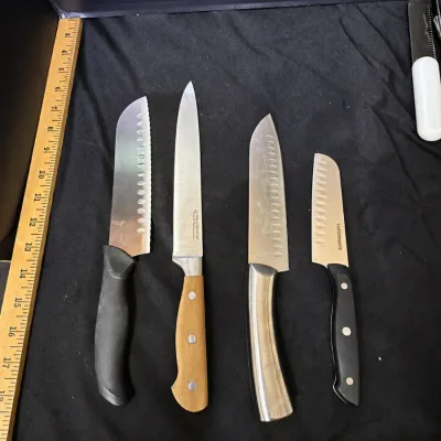 Collection of four modern stainless steel kitchen knives, including santoku and carving styles with various handles, displayed with...