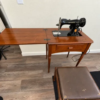 Vintage Singer sewing machine built into a wooden fold-out cabinet, complete with a matching upholstered vanity-style stool.
